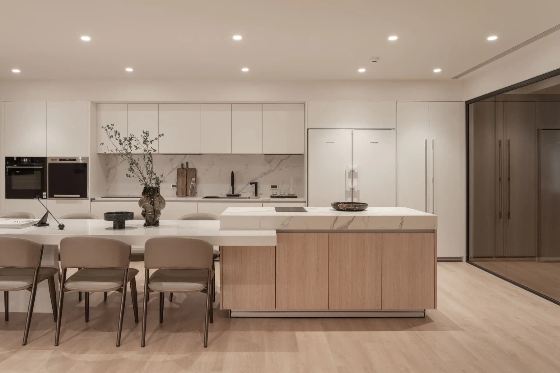 赫里翁 G House 1F開放式中島餐廚區。安頡建築規劃的大型白色賽麗石餐桌連接輕食中島，搭配現代皮革餐椅與嵌入式頂級廚電。